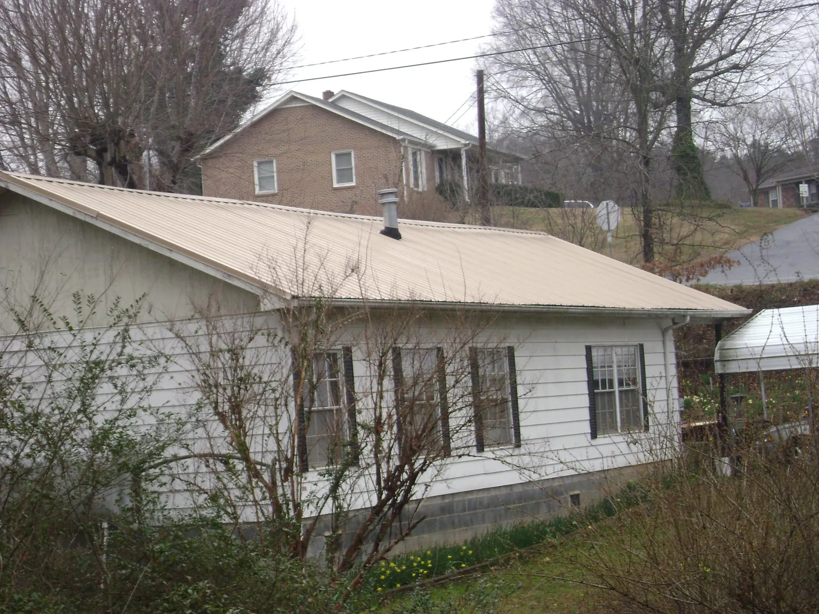Tan metal roof on a white sided house set into a hillside — Commercial Roofing by Roofing Brothers in Grand Junction